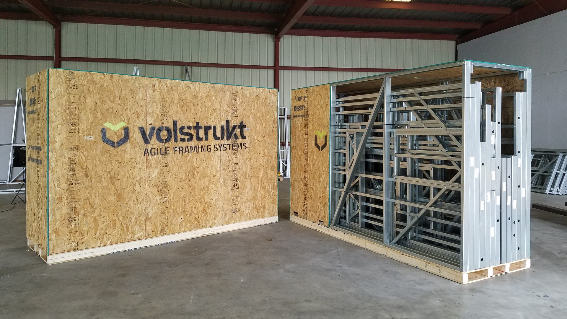 Volstrukt shipping crate beside a rack of pre-assembled galvanized steel wall panels ready for delivery