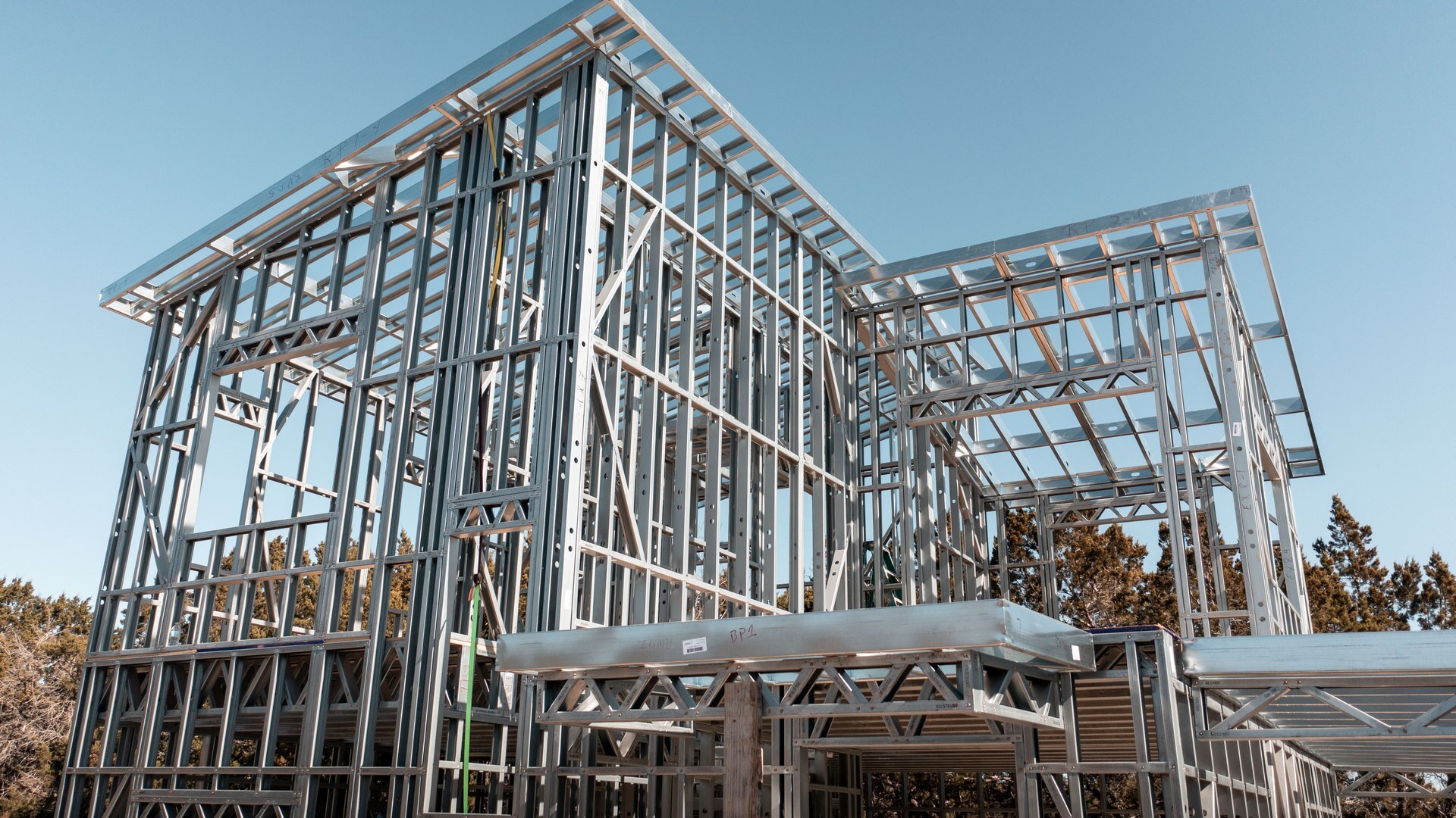 Two-story cold-formed steel frame assembled from pre-built wall panels, seen from below against a blue sky
