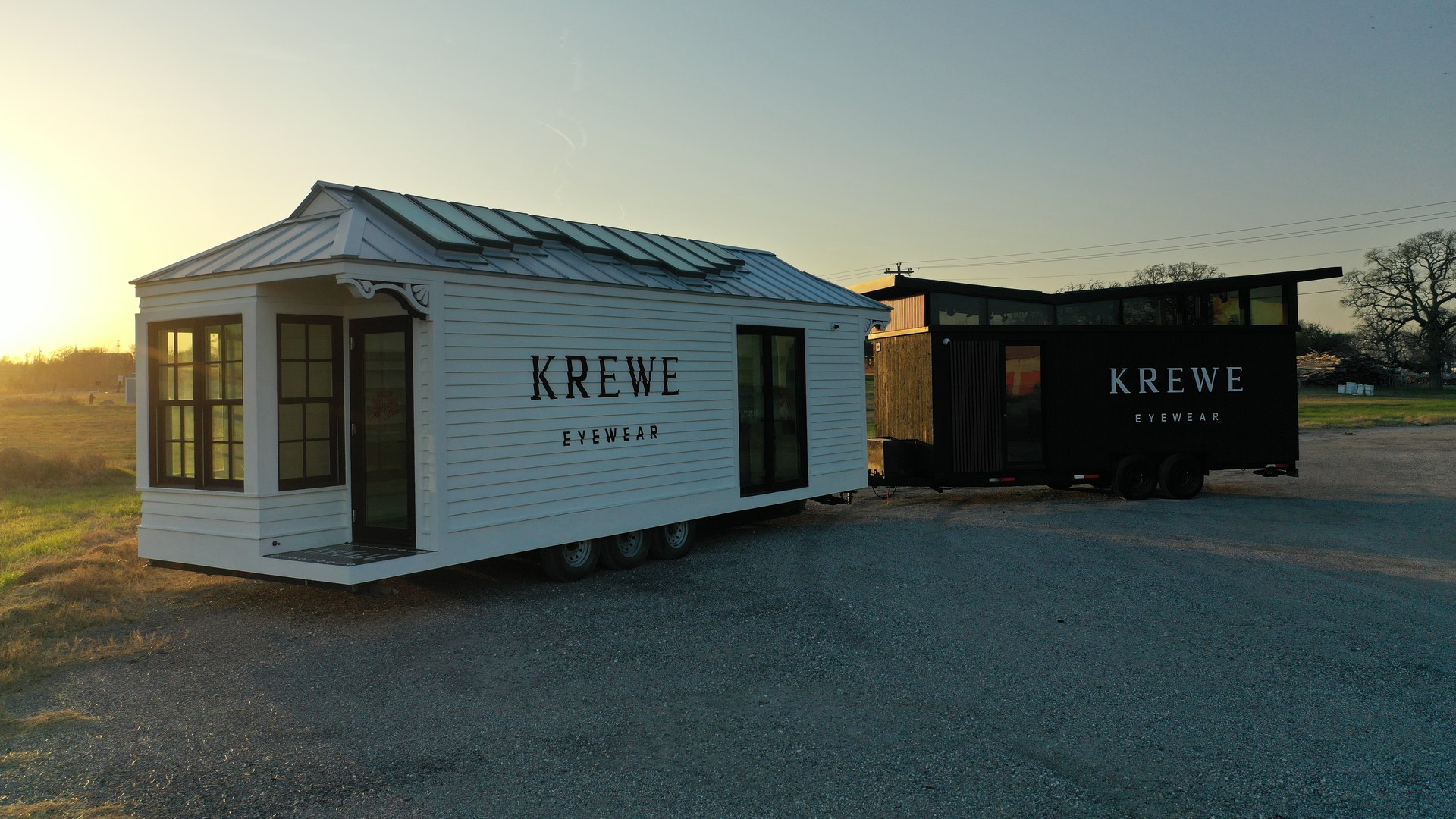 Tiny home on wheels at golden hour on a gravel lot, with a second black tiny home behind it
